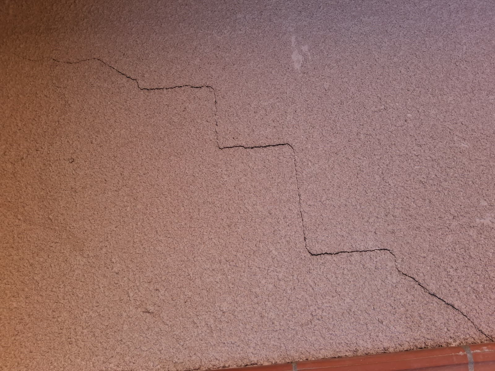 Fissure en escalier sur un enduit de façade, suivant les joints de maçonnerie en marches successives