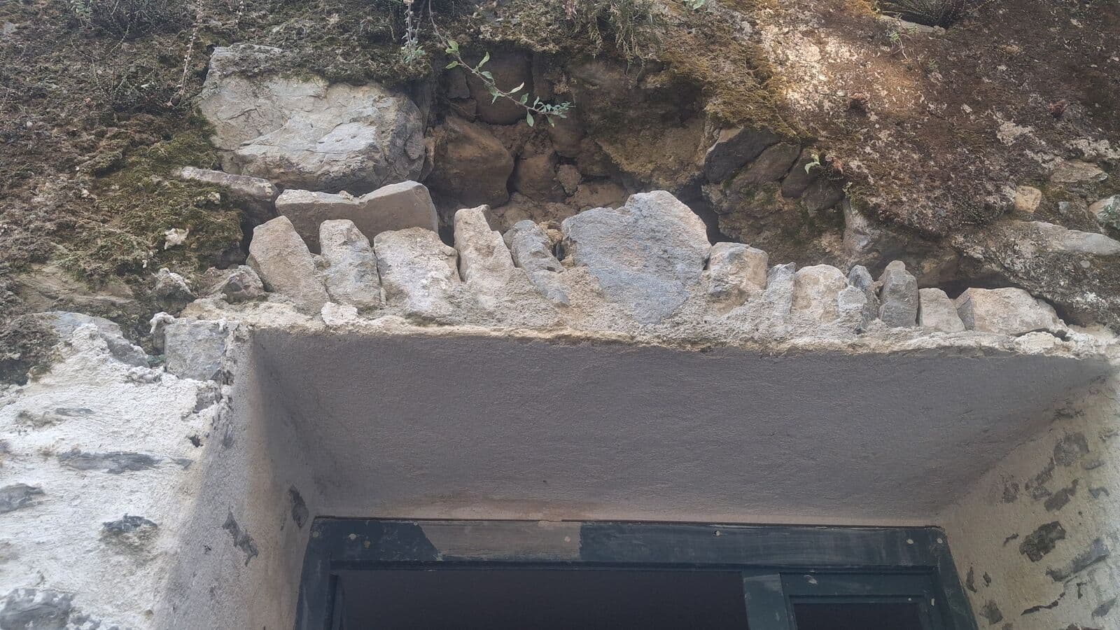 Ouverture percée dans un mur en pierre, pierres simplement empilées au-dessus du passage sans linteau